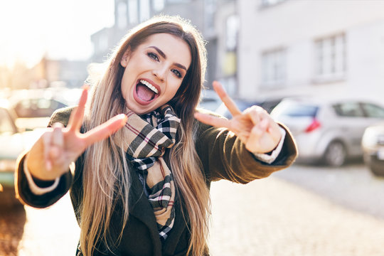 Young woman making peace gesture and smiling at camera on sunny winter day in the city