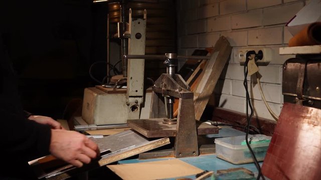 Master is checking result of stamping on a leather detail. He is twisting off plate of handle press machine and getting detail, old hand-operated embossing machine