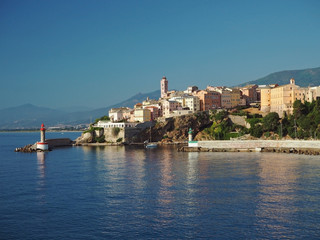 Fototapeta na wymiar Corsica Bastia port view from sea on harbor with red and green lighthous church and old town blue sky background