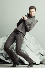 Strike a pose, haute couture concept. Full length portrait of androgynous model with short hair holding lapels, posing over gray background. Pale skin, natural make-up. Futurism style. Studio shot - obrazy, fototapety, plakaty