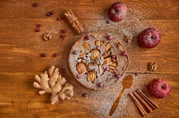 Apple pie with fresh cranberries and walnuts decorated with apples, ginger and cinnamon. Powdered apple pie ready to eat on wooden brown background. General view