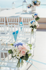 The location of the wedding ceremony on the island of Santorini with white chairs decorated with bouquets of flowers vertical