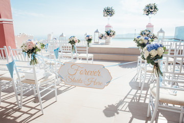The location of the wedding ceremony on the island of Santorini with white chairs decorated with bouquets of flowers