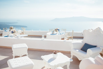 Place for a wedding dinner on the island of Santorini with white tables and armchair and sea view - obrazy, fototapety, plakaty
