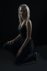 Obraz na płótnie Canvas Beautiful blond woman in denim and black top kneeling in dark with selective lighting