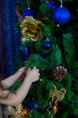 Hands of little girl decorating christmas tree by blue balls.
