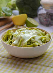 Tasty green macaroni with sour cream sauce on the white wood table. 