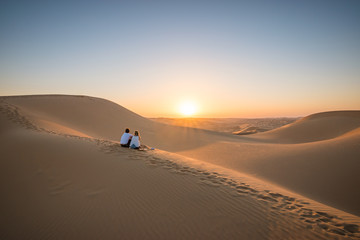 Desert landscape with young couple looking at sunset.