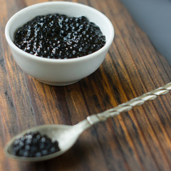 Fresh black caviar in a metal spoon on wooden board.