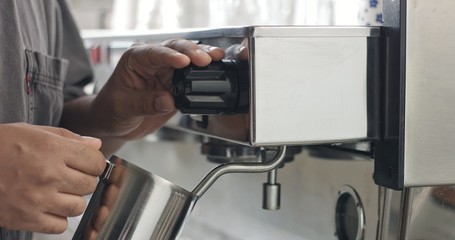 Barista steaming milk or hot cocoa in a stainless steel tumbler on an industrial espresso machine