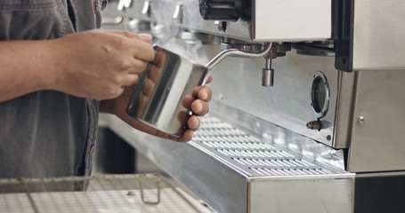Barista steaming milk or hot cocoa in a stainless steel tumbler on an industrial espresso machine