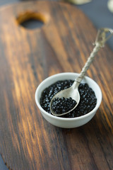 Metal spoon with fresh black caviar over the wooden board.