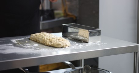 Dark skinned male chef in a black apron works with bread dough in an industrial looking kitchen