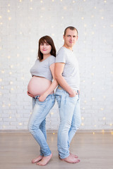 parenthood concept - full length portrait of cute pregnant couple over white brick wall