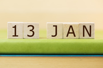 Wooden cube shape calendar for JAN 13 on green book, table. 