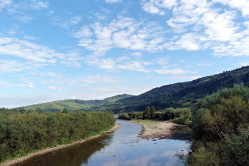Fototapeta na wymiar Panorama of the cloudy sky above the mountain forests and the river in the Ukrainian Carpathians.