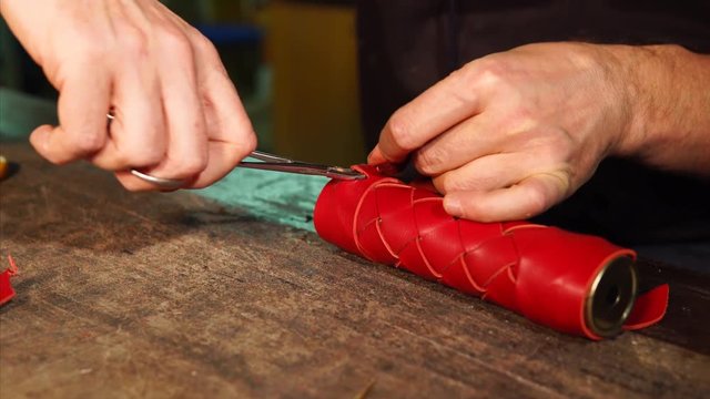 Hands of man is locking border of leather case, using scissors. Craftsman is finishing his exclusive handmade product for customer