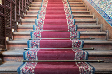 Front view of old ascending wooden stairs with ornate red carpet and wooden balustrade