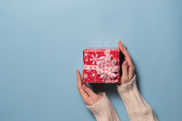 Female hand keeping red box with gift over blue background