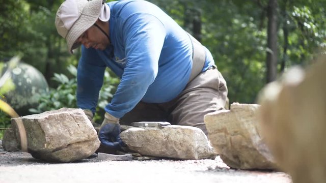 Using shale shims, a mason levels out large rocks for construction of a rock wall.