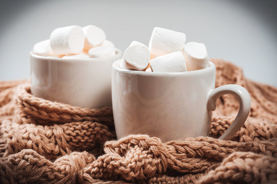 Cocoa or coffee with marshmallows in a white cup with a brown knitted winter scarf. Beautiful christmas background