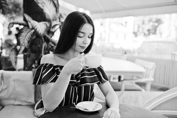 Gorgeous brunette girl sitting on the table in cafe with cup of coffee.