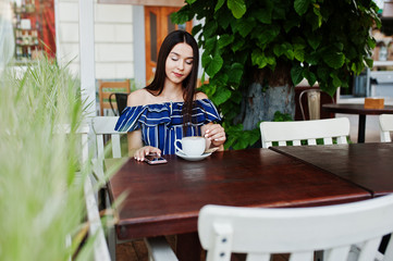 Gorgeous brunette girl sitting on the table in cafe with cup of coffee and using phone.