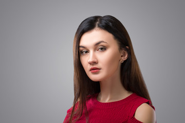 Fototapeta premium Ładna brunetka kobieta w czerwonej sukience na szarym tle.