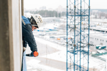construction worker in safety protective equipment with drill working on height.