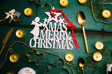 Christmas luxury holiday concept, with a plate with text impressed " merry christmas" ,xmas balls and gold decoration over a green metallic background, top view from above.