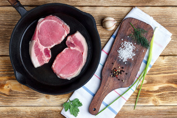 Raw pork meat steak on vintage cast ironl pan, cutting board and spices on wooden rustic background.