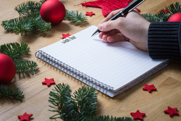 Writing a wish list for Christmas on a notepad with Christmas decorations and fir branches on a...