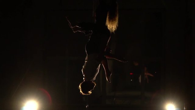 A man in a suit and a woman with long hair hanging from the crossbar for aerial acrobatics, slow motion