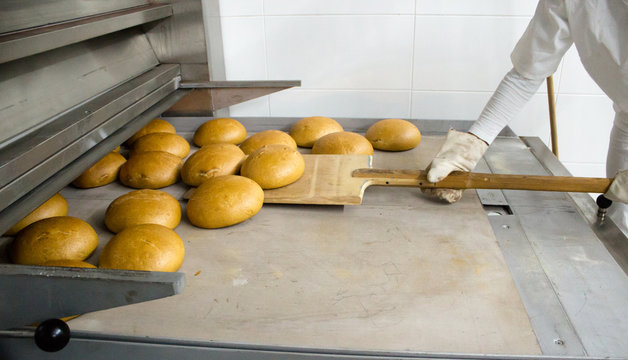 Baker woman getting bread out of bakery oven in her bakery