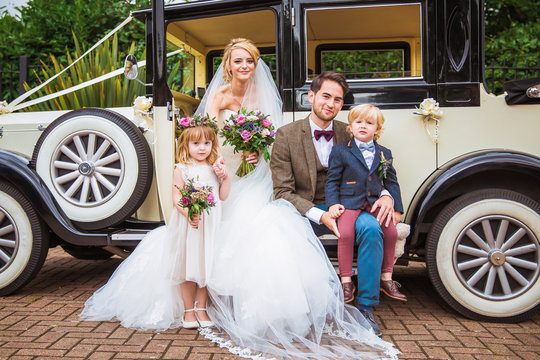 The young happy beautiful newlyweds sitting on a car with charming children