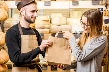 Salesman packing shopping bag with goods and giving to the woman customer at the cheese shop