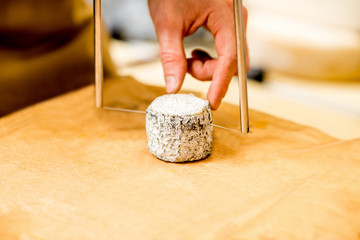 Cutting with wire slicer a young goat cheese at the food store. Close-up view