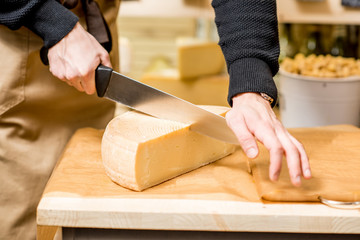 Cutting with wire slicer a seasoned cheese at the food store. Close-up view