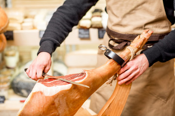 Cutting with long knife prosciutto leg in the food store