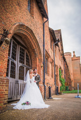 Obraz premium The young beautiful smiling newlyweds standing in embrace before the door of building outdoor and looking aside