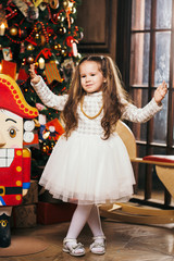 Cute little girl dancing near Christmas tree and nutcracker