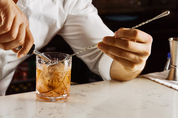 Charming barman elegantly prepares a mixed drink by pouring all the ingredients into a bar spoon.