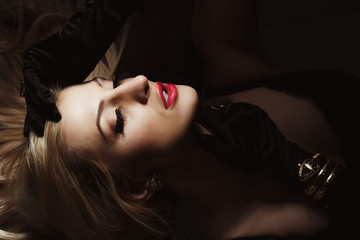 Closeup portrait of seductive blonde woman with bright makeup wears silk gloves and gold jewelry posing in the shadows