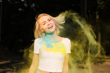 Happy young woman in white t shirt with hair in wind playing with exploding Holi powder