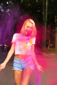 Happy young woman in white t shirt and jeans shorts posing with red Holi powder