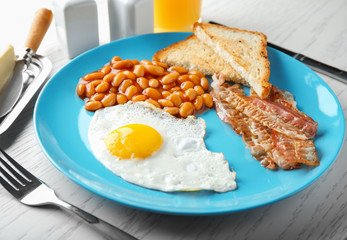 Plate with fried egg, bacon and beans on wooden table