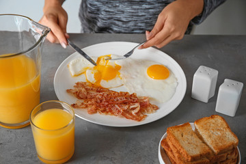 Young woman eating fried eggs and bacon at table