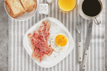Plate with fried egg and bacon on table