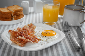 Plate with fried egg and bacon on table