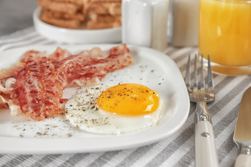 Plate with fried egg and bacon on table